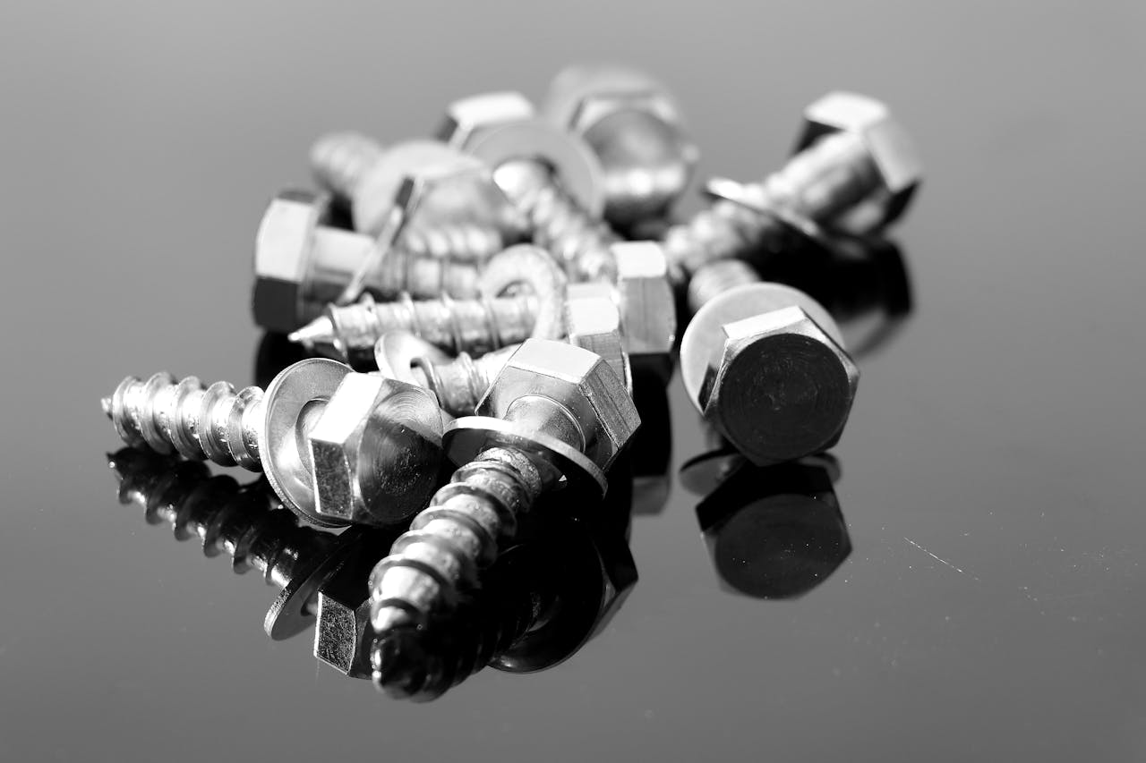 about-us Close-up black and white photo of metal screws on reflective surface.