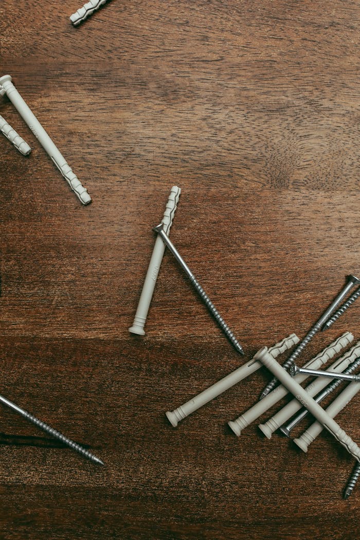 Flat lay image of screws and plastic anchors scattered on a wooden surface, perfect for DIY projects.